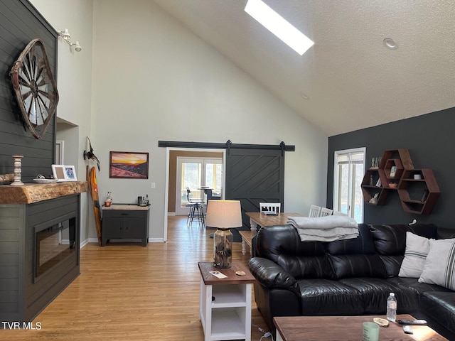 living room with high vaulted ceiling, a textured ceiling, a barn door, and light hardwood / wood-style flooring