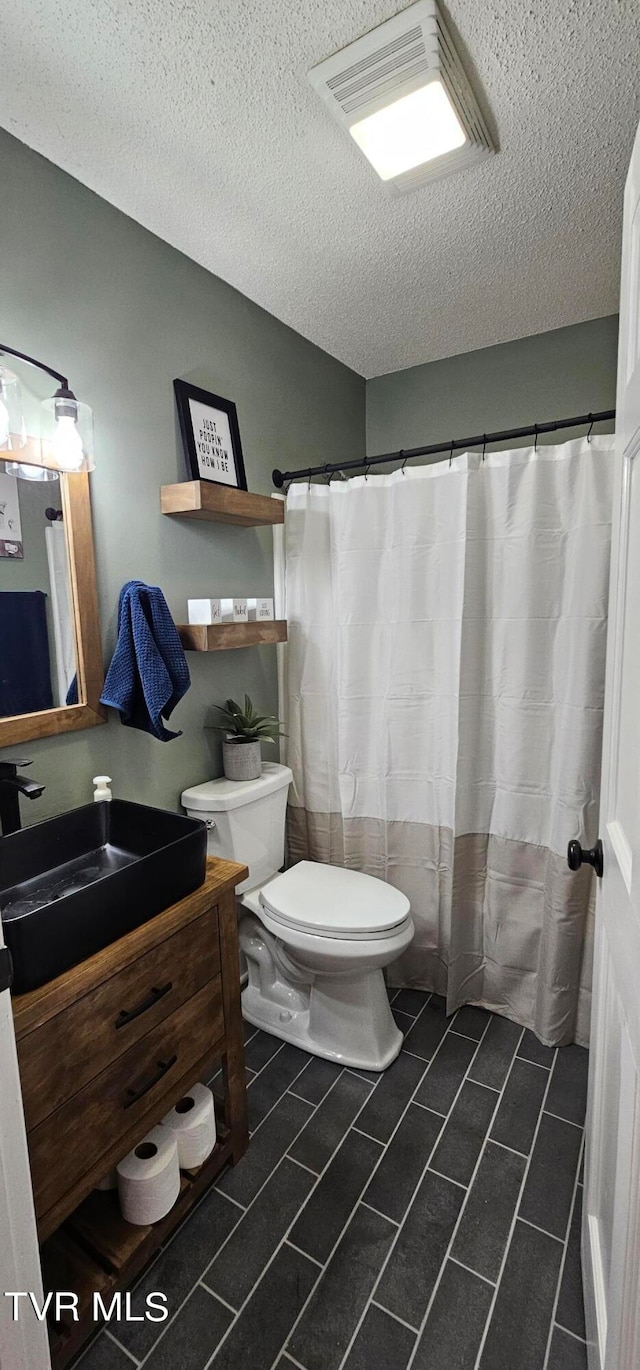 bathroom featuring a textured ceiling, toilet, large vanity, and tile floors