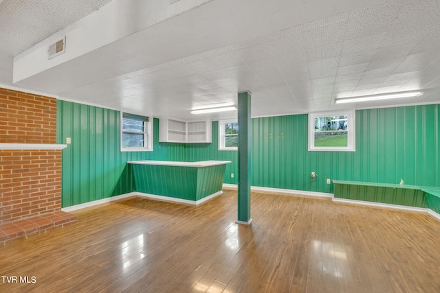 basement featuring brick wall, plenty of natural light, and light wood-type flooring