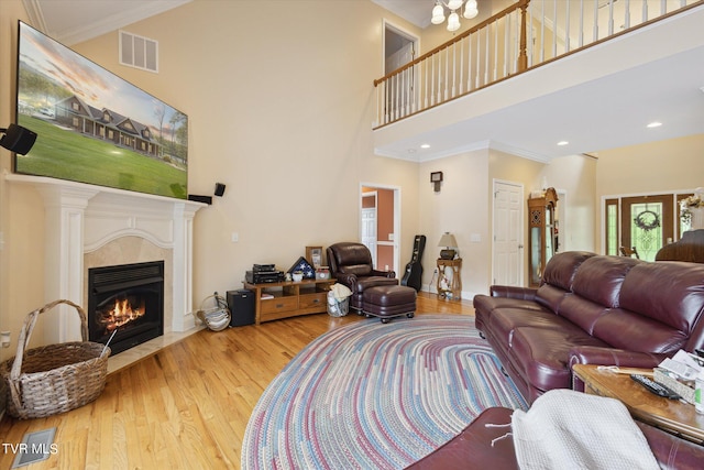 living room with a towering ceiling, light hardwood / wood-style floors, and ornamental molding