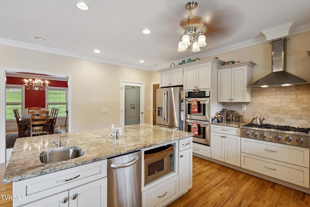 kitchen featuring appliances with stainless steel finishes, wall chimney range hood, a center island with sink, sink, and light hardwood / wood-style floors