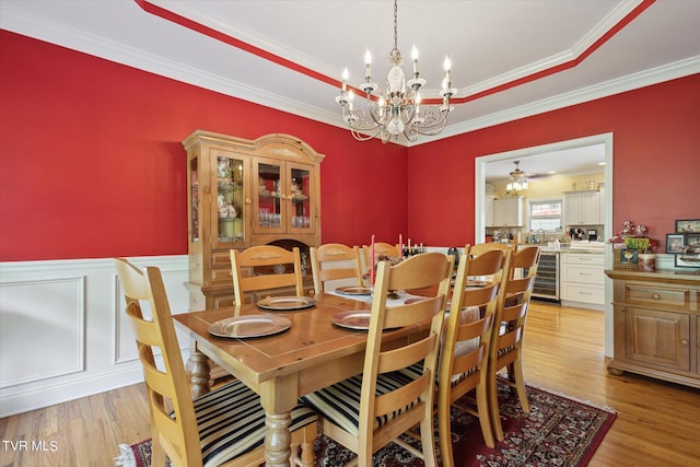 dining space featuring a tray ceiling, light hardwood / wood-style flooring, crown molding, and beverage cooler