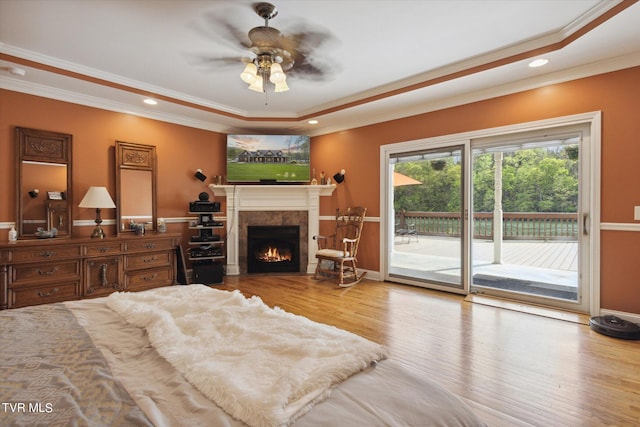 bedroom featuring ceiling fan, a fireplace, access to exterior, a tray ceiling, and light hardwood / wood-style flooring