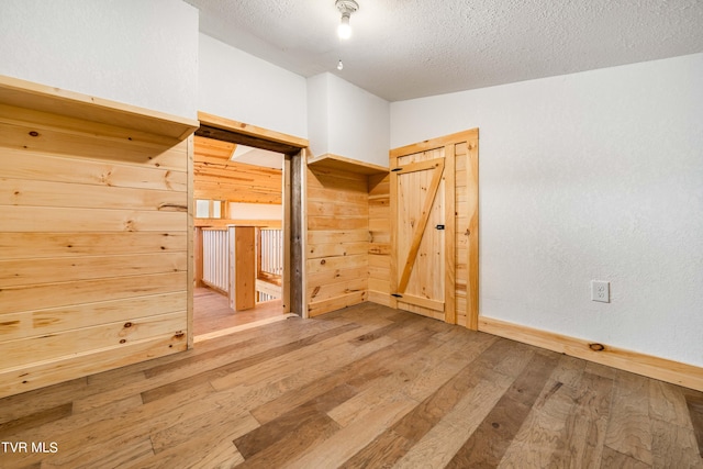 unfurnished bedroom featuring wooden walls, a textured ceiling, and light wood-type flooring