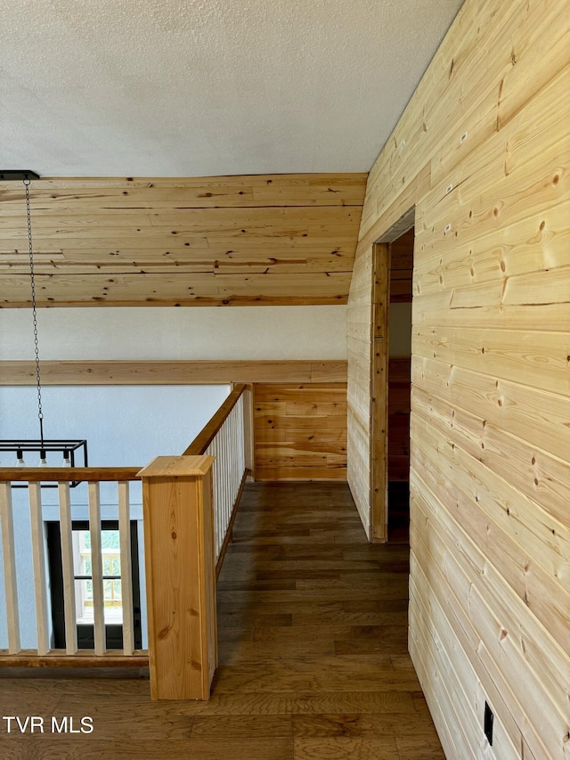 corridor featuring wood walls, a textured ceiling, hardwood / wood-style flooring, and a notable chandelier