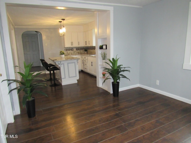 kitchen featuring decorative light fixtures, backsplash, light stone counters, white cabinets, and dark hardwood / wood-style flooring