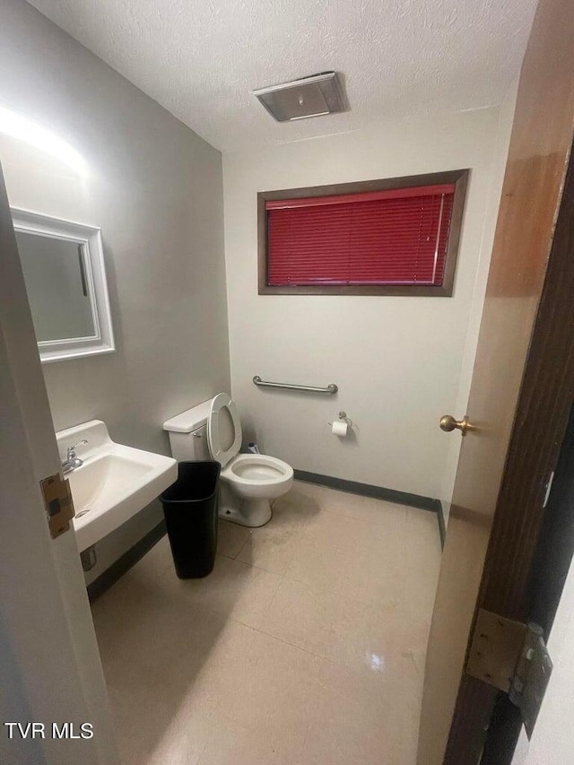 bathroom featuring tile flooring, sink, toilet, and a textured ceiling