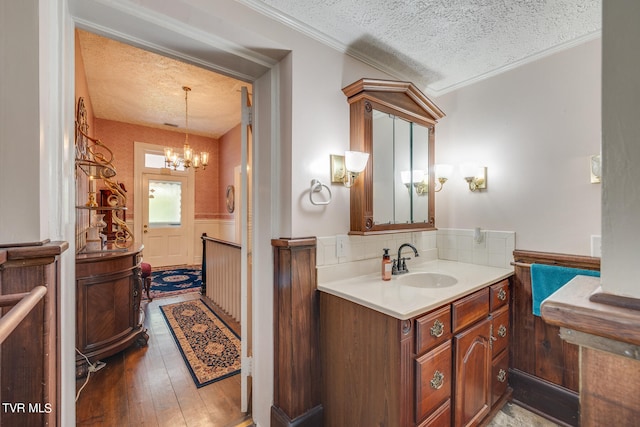 bathroom with a textured ceiling, a chandelier, ornamental molding, wood-type flooring, and vanity