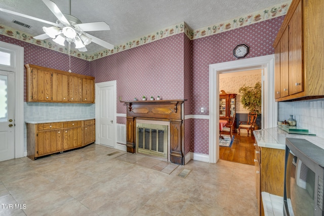 kitchen with ceiling fan, tile counters, light tile floors, and a textured ceiling