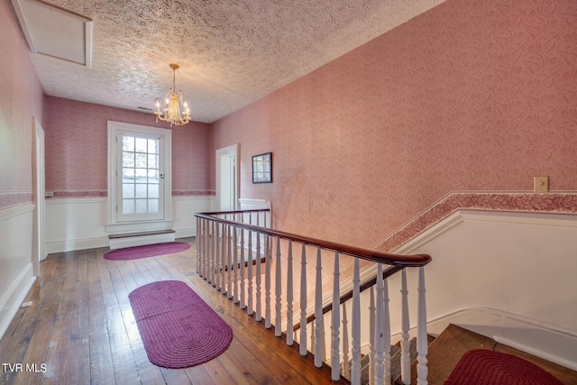 hall featuring wood-type flooring, an inviting chandelier, and a textured ceiling