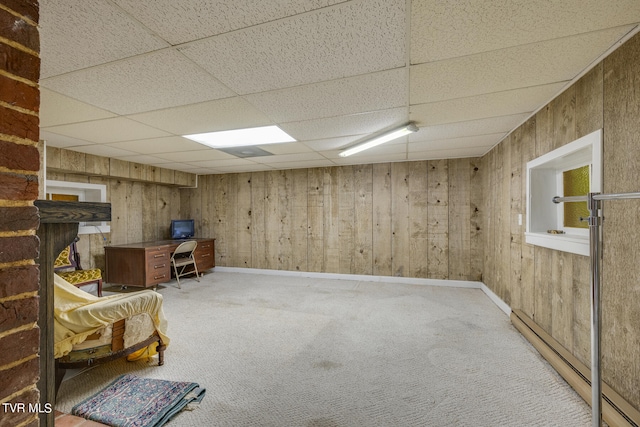 basement with a drop ceiling, carpet, wooden walls, and a baseboard radiator