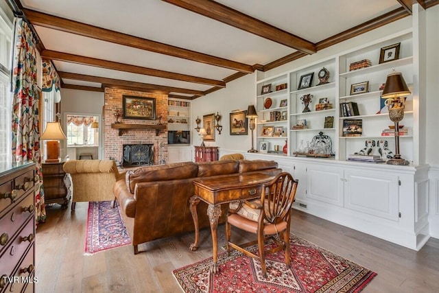 living room with built in features, a fireplace, beam ceiling, brick wall, and hardwood / wood-style flooring