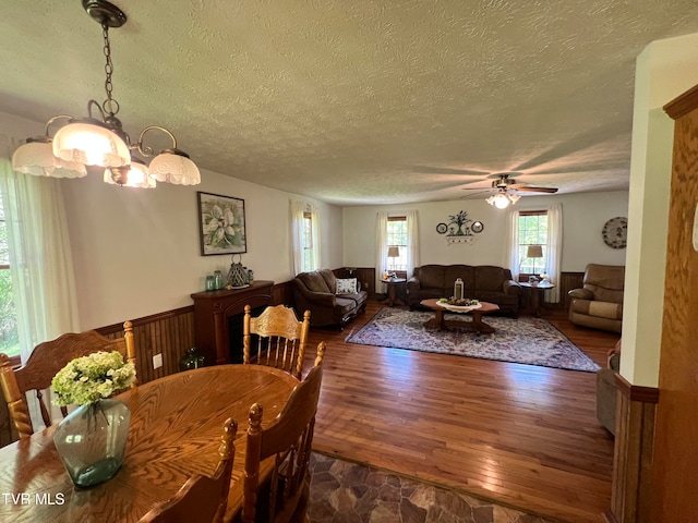 dining space featuring hardwood / wood-style flooring, ceiling fan with notable chandelier, and a textured ceiling