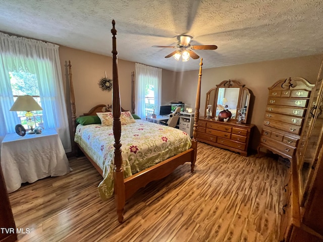 bedroom with hardwood / wood-style floors, ceiling fan, and a textured ceiling