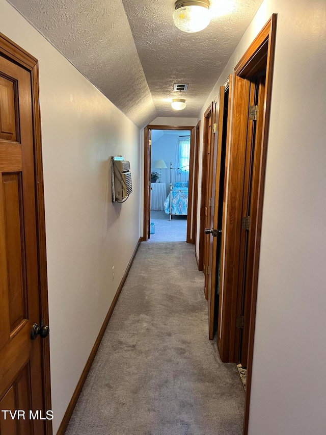 hall with lofted ceiling, carpet, and a textured ceiling