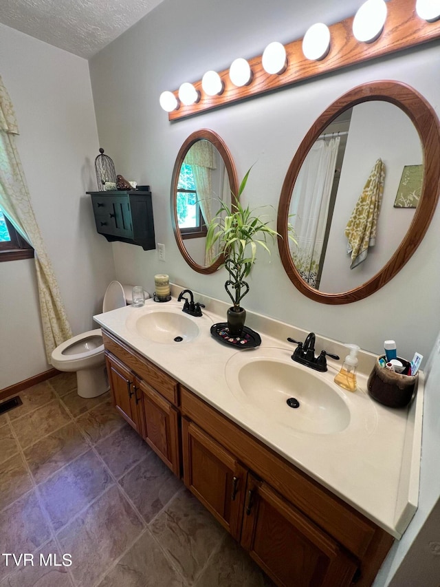 bathroom featuring toilet, tile flooring, a textured ceiling, and double sink vanity