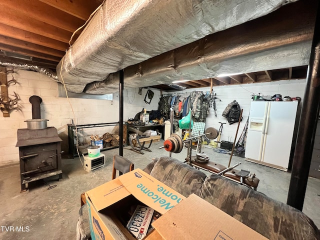 basement featuring a wood stove and white fridge with ice dispenser