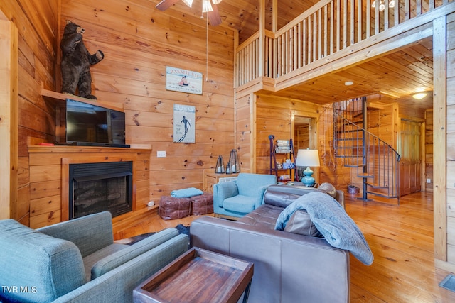 living room with wood walls, a high ceiling, ceiling fan, and light wood-type flooring