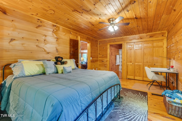 bedroom with light hardwood / wood-style flooring, wooden ceiling, wood walls, a closet, and ceiling fan