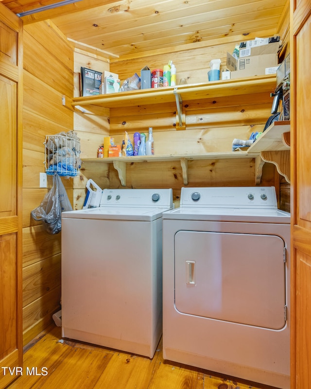 laundry area with light hardwood / wood-style floors, wood ceiling, washer and clothes dryer, and wood walls