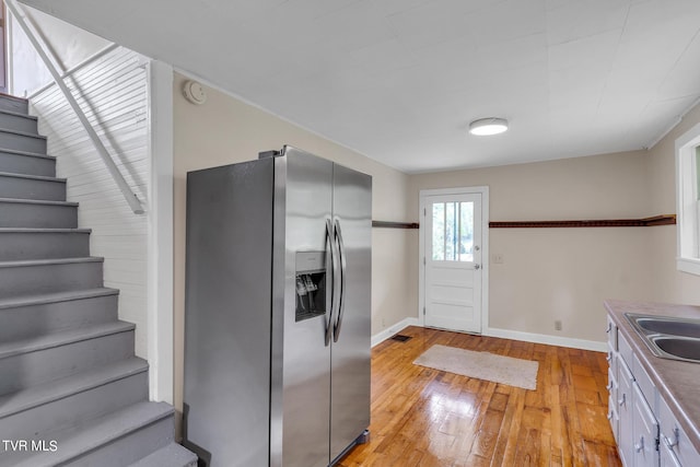 kitchen with sink, light hardwood / wood-style floors, white cabinetry, and stainless steel refrigerator with ice dispenser