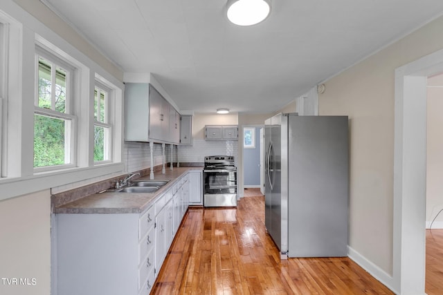 kitchen with tasteful backsplash, stainless steel appliances, sink, and light wood-type flooring