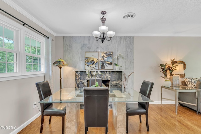 dining space with a fireplace, a notable chandelier, light hardwood / wood-style flooring, and crown molding