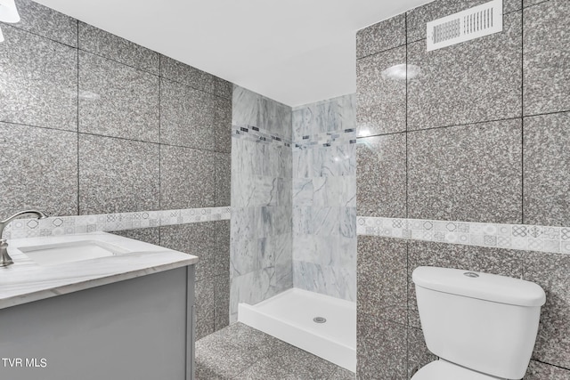 bathroom featuring tiled shower, tile walls, toilet, and vanity