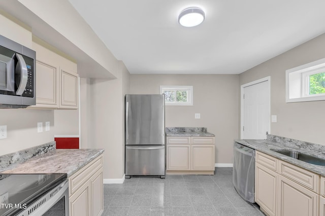 kitchen featuring light stone countertops, light tile flooring, cream cabinetry, sink, and appliances with stainless steel finishes