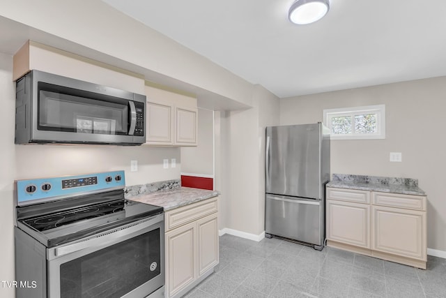 kitchen with light stone countertops, stainless steel appliances, cream cabinetry, and light tile floors