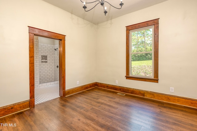 spare room with an inviting chandelier and dark wood-type flooring