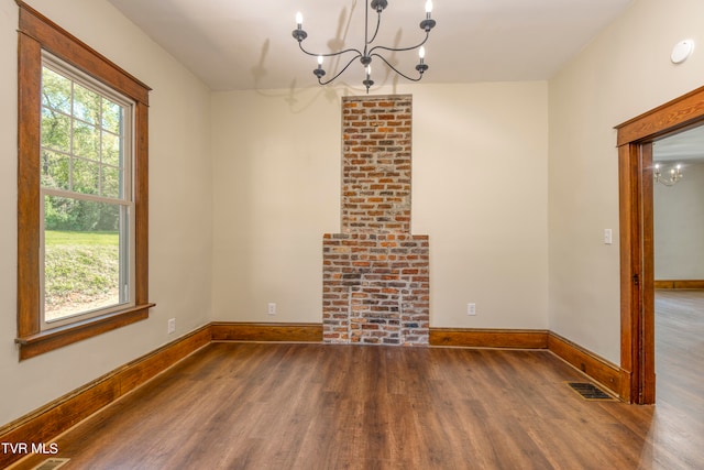 empty room with dark hardwood / wood-style flooring, brick wall, and an inviting chandelier