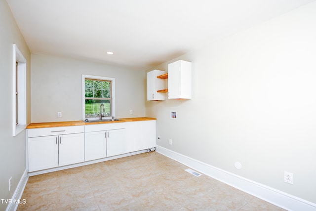 interior space featuring hookup for an electric dryer, hookup for a washing machine, light tile floors, sink, and cabinets