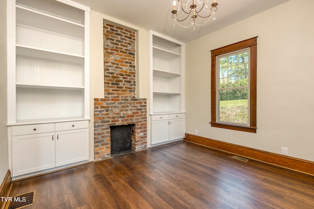 unfurnished living room with a fireplace, dark wood-type flooring, an inviting chandelier, and brick wall