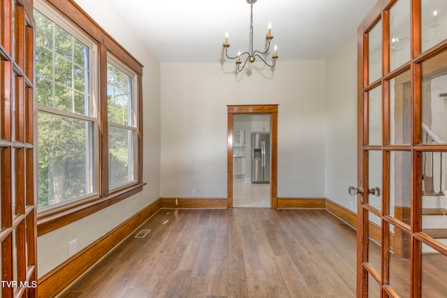 empty room with french doors, a chandelier, and hardwood / wood-style flooring