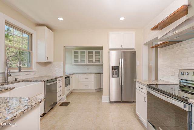 kitchen featuring white cabinets, backsplash, appliances with stainless steel finishes, wall chimney range hood, and light tile floors