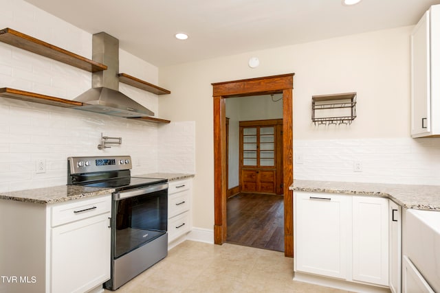 kitchen featuring stainless steel electric stove, white cabinets, wall chimney range hood, light tile floors, and tasteful backsplash