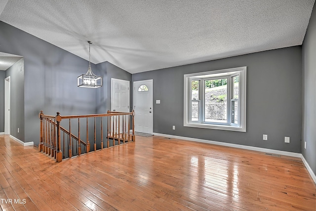 entryway featuring a notable chandelier, lofted ceiling, a textured ceiling, and light hardwood / wood-style flooring