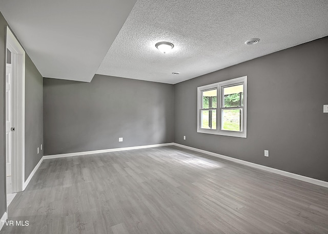 spare room featuring light wood-type flooring and a textured ceiling