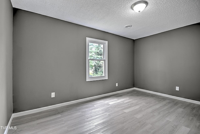 empty room with a textured ceiling and light hardwood / wood-style flooring