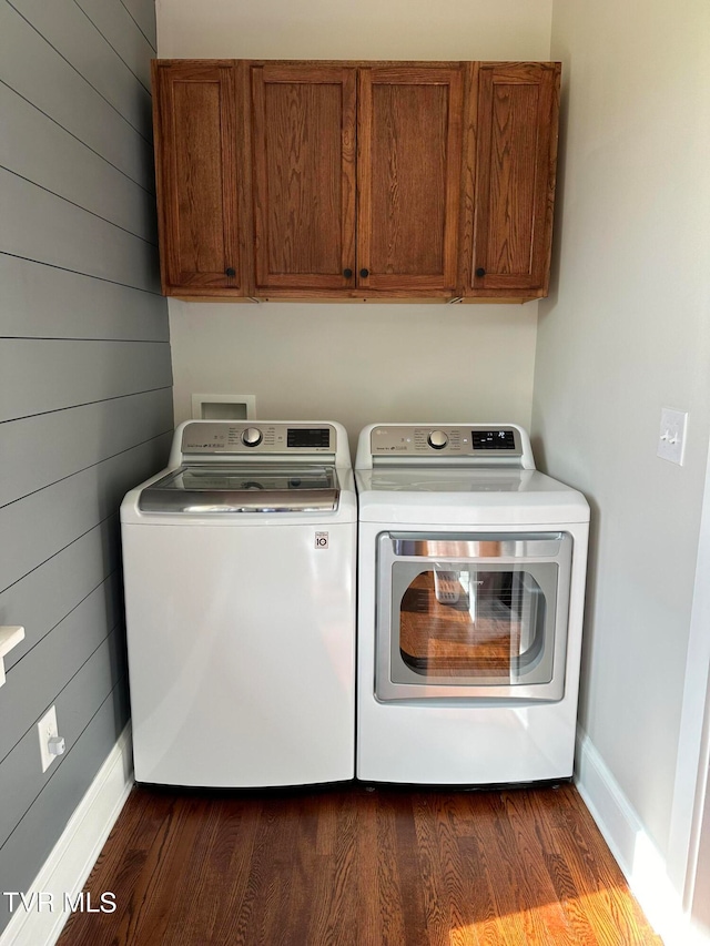 laundry room featuring cabinets, dark hardwood / wood-style floors, washer and dryer, and wooden walls