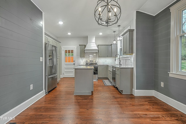 kitchen with backsplash, custom range hood, stainless steel appliances, a kitchen island, and hanging light fixtures