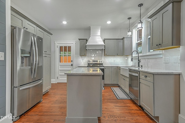 kitchen featuring custom exhaust hood, gray cabinets, appliances with stainless steel finishes, a kitchen island, and light stone counters