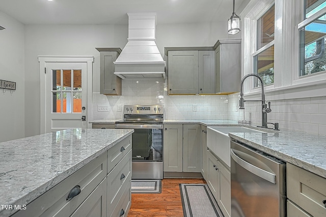 kitchen with custom exhaust hood, backsplash, hanging light fixtures, gray cabinets, and appliances with stainless steel finishes