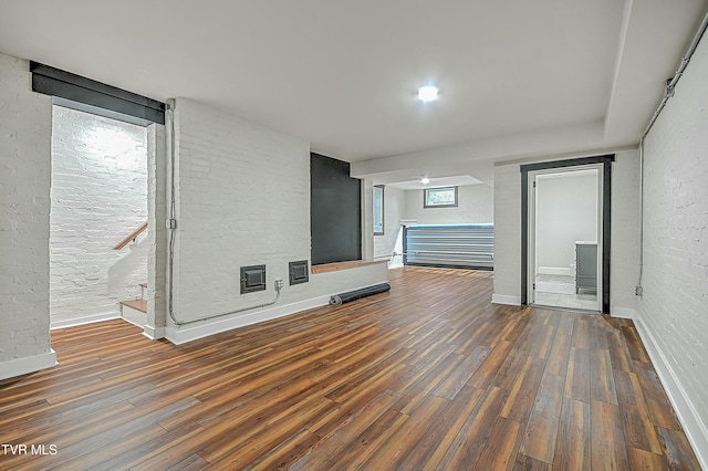 unfurnished living room with dark hardwood / wood-style flooring and brick wall