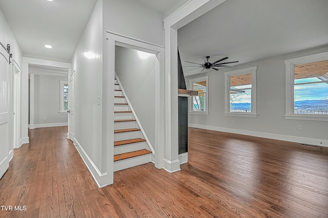 stairway featuring a barn door, hardwood / wood-style flooring, ceiling fan, and a healthy amount of sunlight