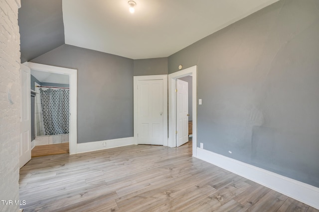 interior space featuring lofted ceiling, brick wall, and light wood-type flooring