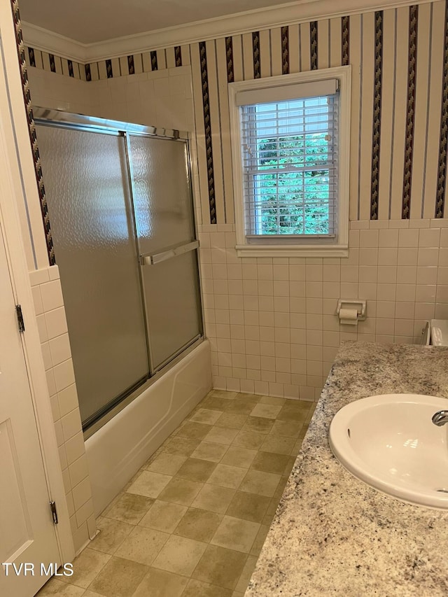 bathroom with tile flooring, combined bath / shower with glass door, tile walls, ornamental molding, and vanity