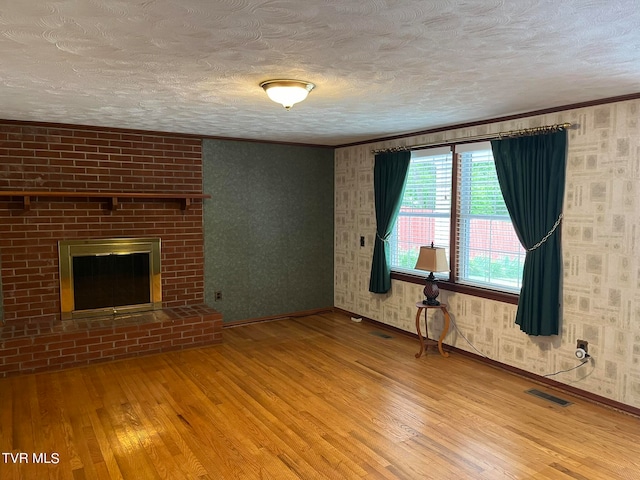 unfurnished living room with a textured ceiling, ornamental molding, hardwood / wood-style flooring, and a fireplace