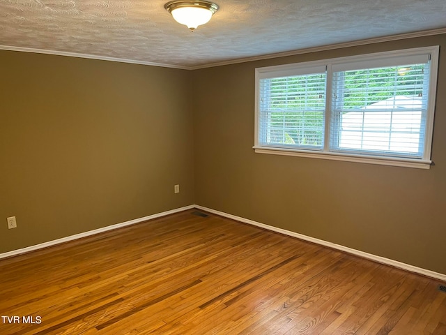 empty room with a textured ceiling, ornamental molding, and hardwood / wood-style floors